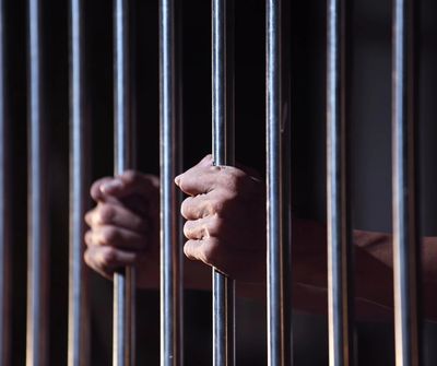 Man's hands clenching prison bars
