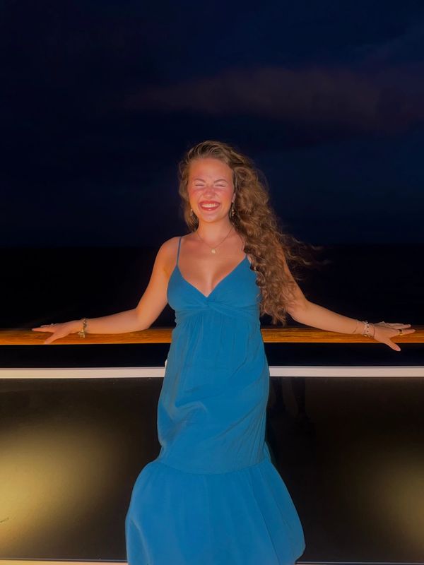 A woman in a blue dress smiles brightly on a night deck.