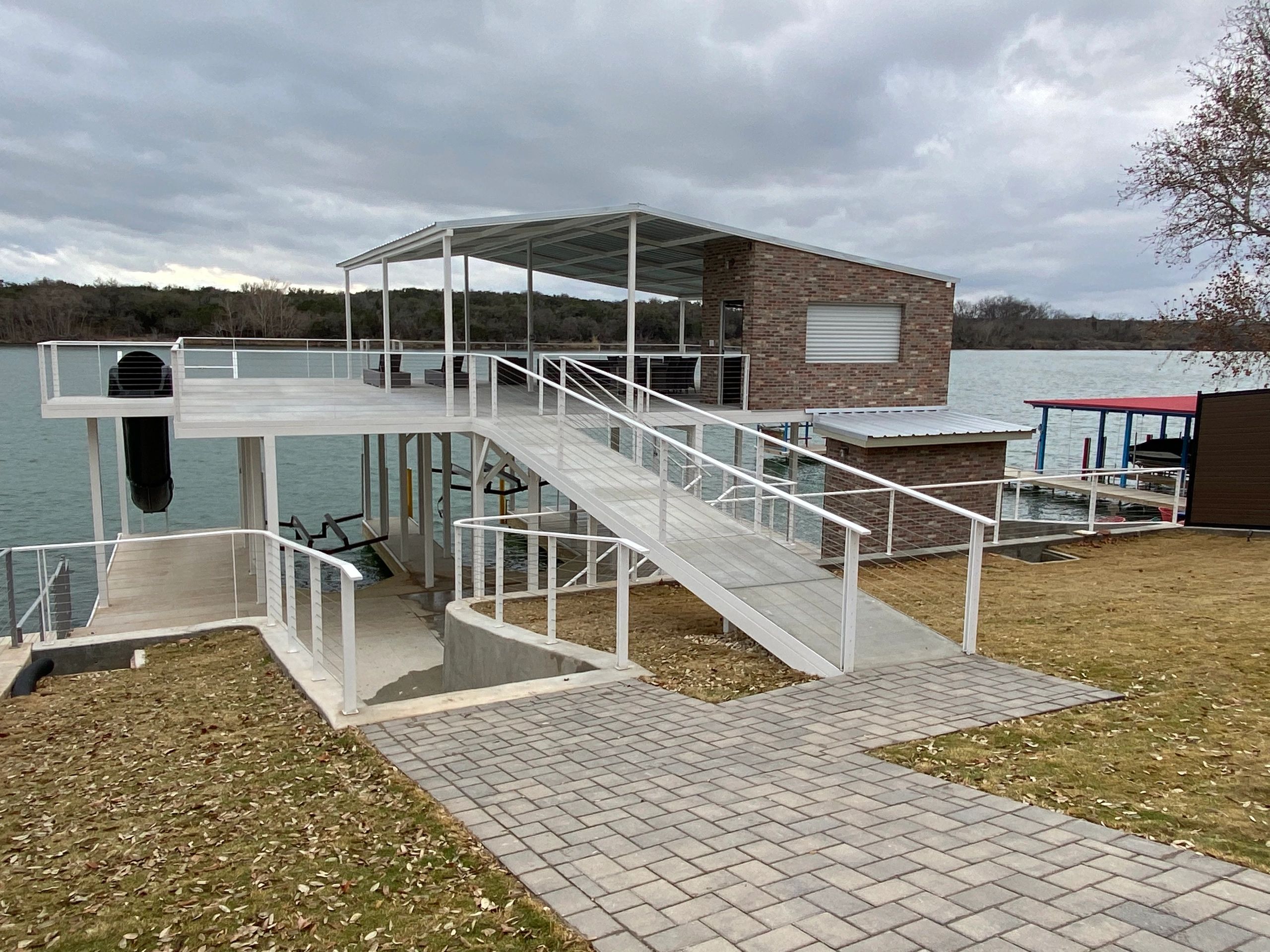 A modern covered dock with a slide on a lake under a cloudy sky.