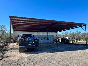 Metal carport with vehicles and a shipping container underneath.