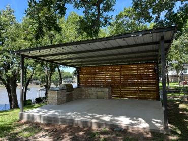 Covered outdoor concrete space with grill and wooden backdrop.