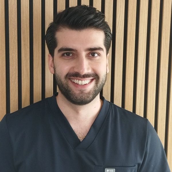 Smiling man in dark scrubs with wooden panel background.