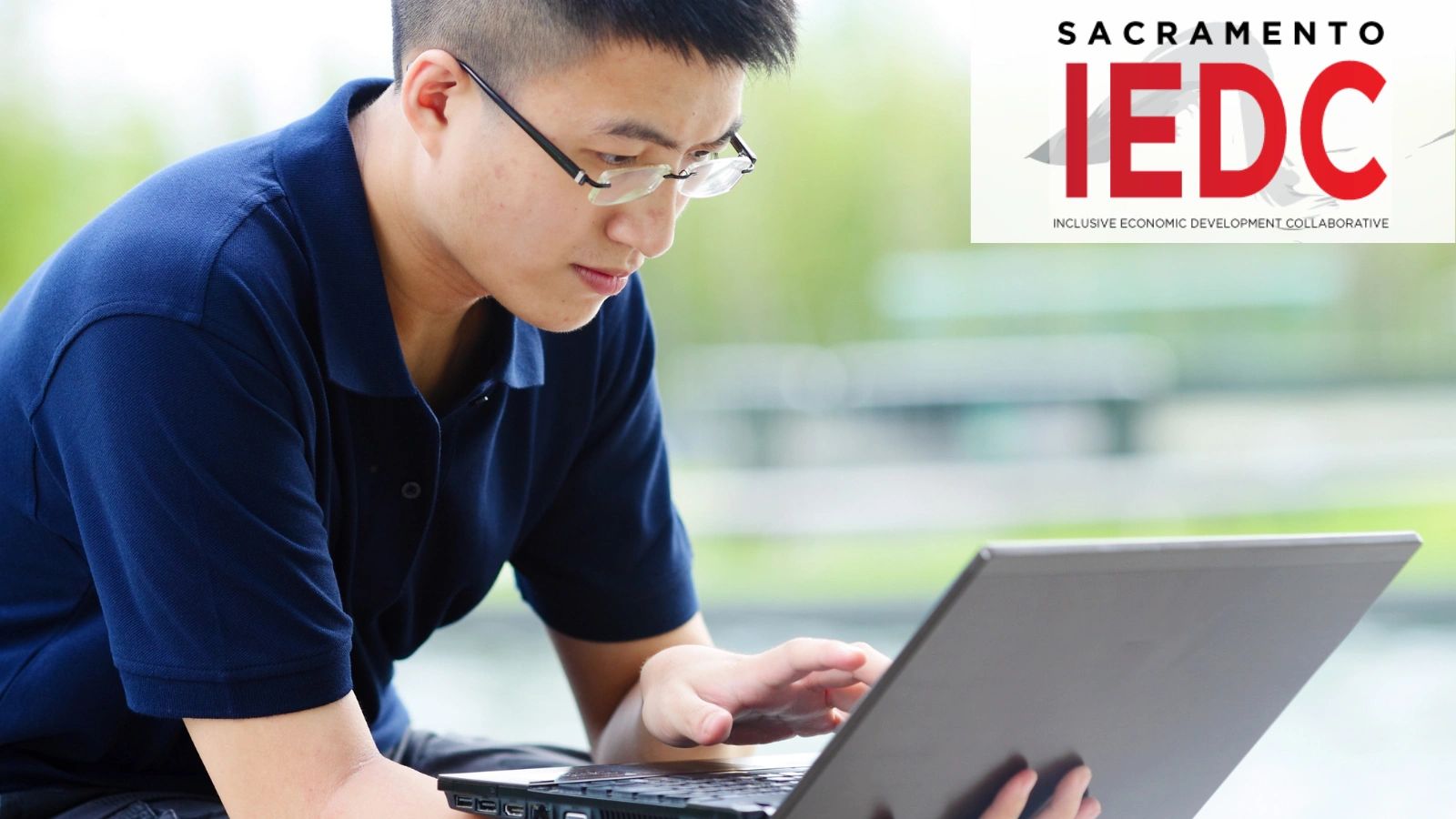 Young man focused on laptop work with Sacramento IEDC logo in background.