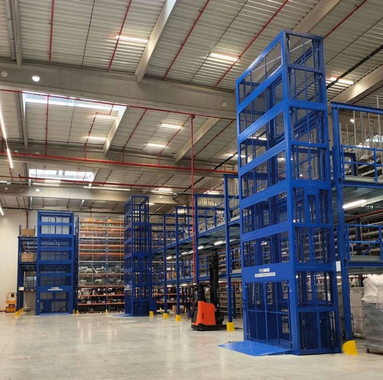 Modern warehouse interior with tall blue storage racks and a forklift.
