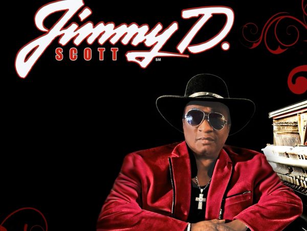 Musician Jimmy D. Scott in a red velvet jacket and hat by a piano.
