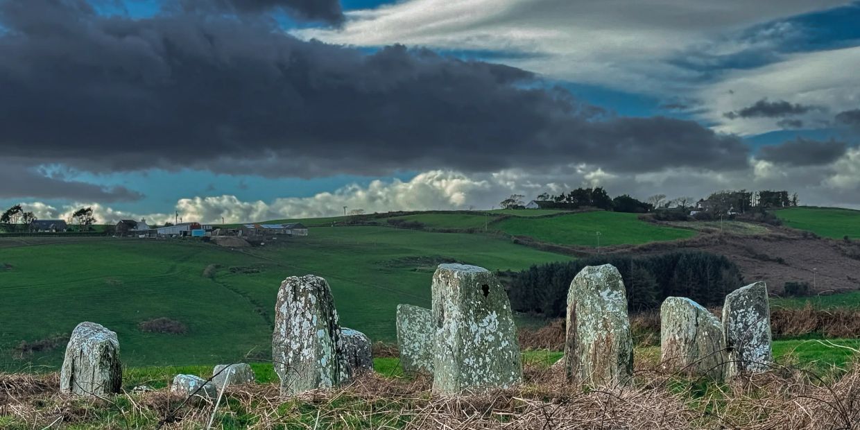 Ancient standing stones on a grassy hillside under a dramatic cloudy sky.