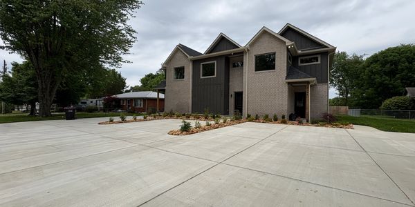 Modern two-story house with large concrete driveway on cloudy day.