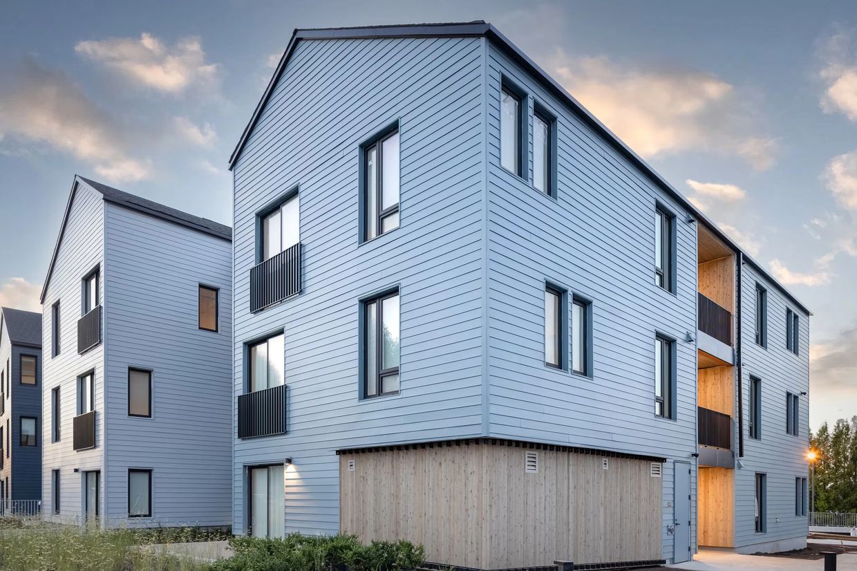 Modern blue apartment buildings with wooden accents under a cloudy sky.