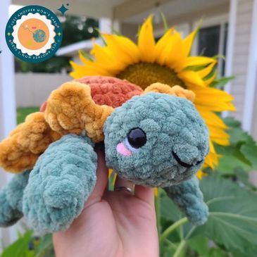 Crocheted sea turtle with a sunflower shaped shell posed in front of a sunflower