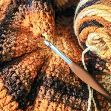 Brown crochet hook ontop of fall colored crocheted yarn piece