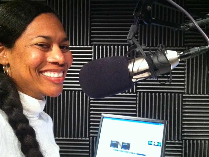 Smiling woman speaking into a microphone in a soundproof room.