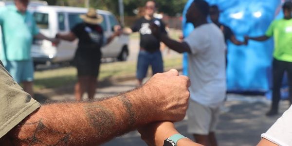 People holding hands in a supportive circle outdoors.
