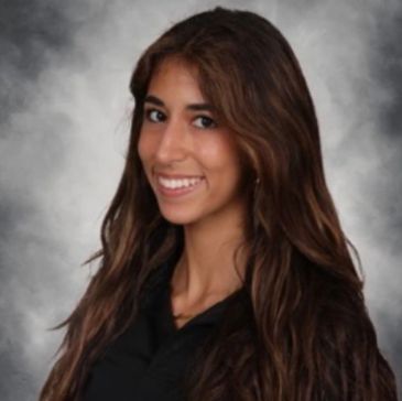 A young woman with long brown hair smiling against a gray backdrop.