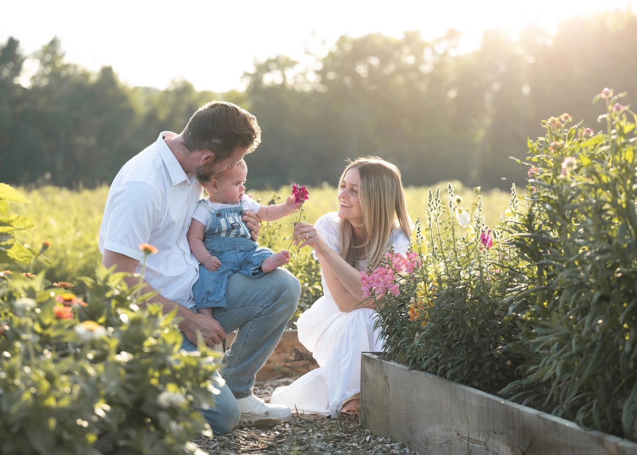 A happy family enjoys flowers together in a sunlit garden.