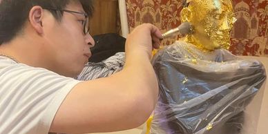 A man applies gold leaf to a statue's head and shoulders.