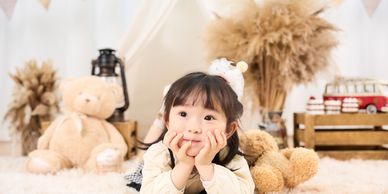 Adorable little girl lying on a fluffy rug surrounded by teddy bears and cozy decor.