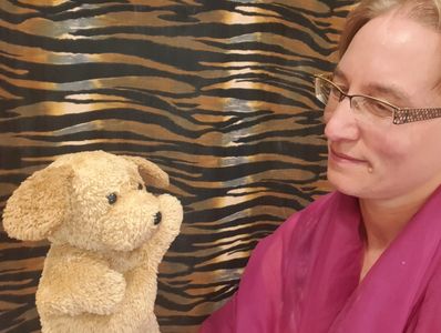 Person looking at a puppy puppet with its hand raised as if asking a question.