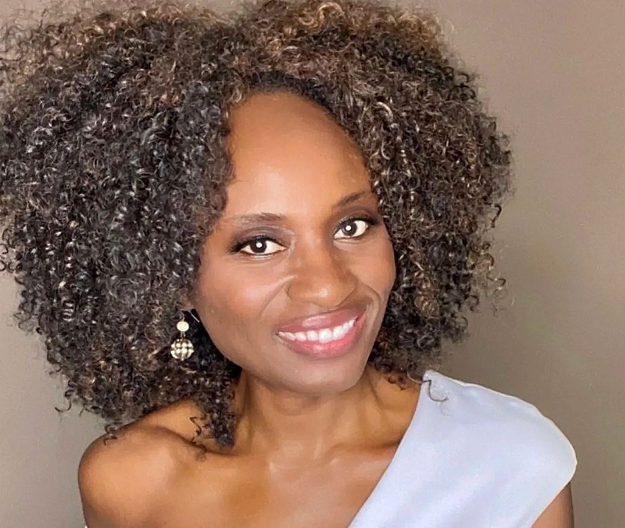 Smiling woman with curly hair and elegant earrings.
