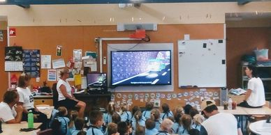 Students in uniform watching a presentation on a screen in a classroom.