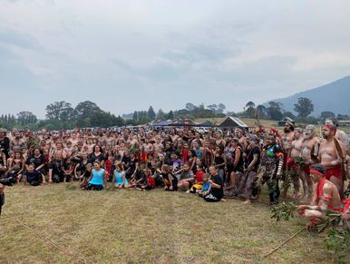 Large group gathered outdoors with some in traditional attire and face paint.