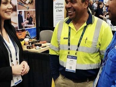 People engaged in a friendly conversation at a trades expo booth.