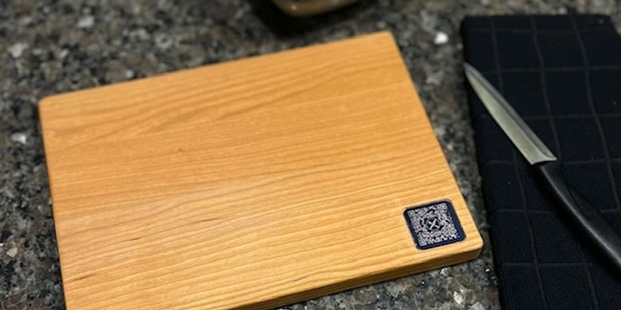 A wooden cutting board on a granite countertop with a knife and black cloth nearby.