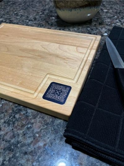 Wooden cutting board with a QR code, knife, and black cloth on granite countertop.