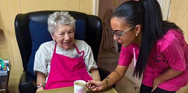 Caregiver offers a cup of tea to an elderly woman in a cozy setting.