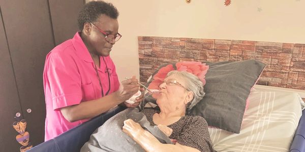 Caregiver feeding an elderly woman in bed with a spoon.