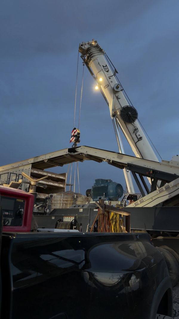 A crane lifting equipment at dusk on a construction site.