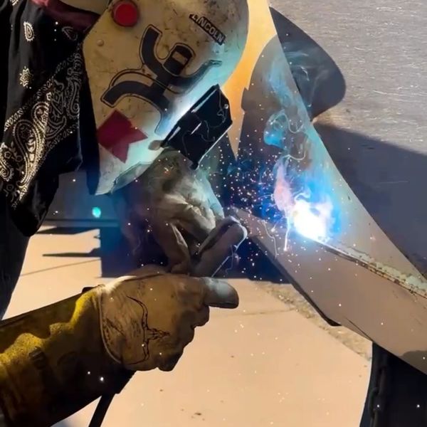 Person welding metal with protective gloves and helmet.