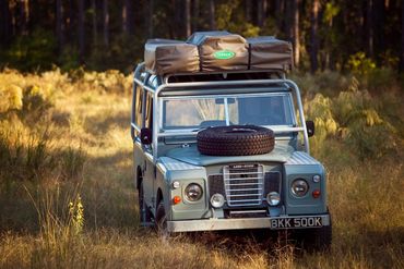 Classic Land Rover with rooftop tent in a grassy wilderness.