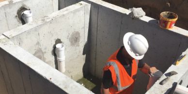 Construction worker inside a concrete structure with pipes.