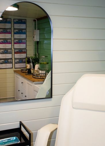 A clean, bright room with a white chair and mirror reflecting certificates and a refreshment area.