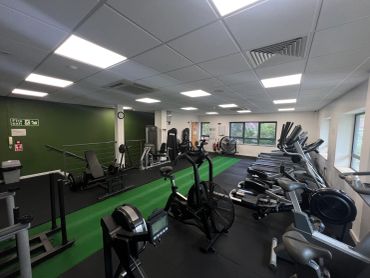 A modern gym with various fitness equipment and green accent wall.