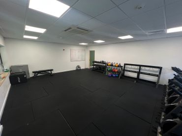 Empty gym room with kettlebells, dumbbells, and workout bench.