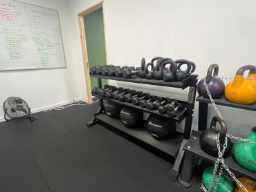 Gym with kettlebells, dumbbells, and a whiteboard workout plan.