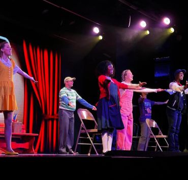 Actors taking a bow on stage with lights and red curtains.