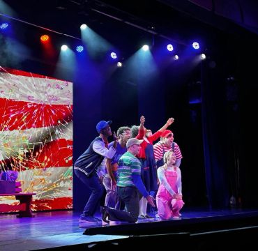 Actors performing on stage with vibrant lighting.