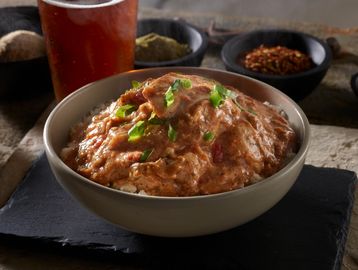 Creamy chicken stew in a big bowl, Pint of Beer in the background, with green and red herbs & spices