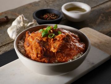 Big bowl of shredded chicken, Voodoo sauce dark red color, pepper flakes, garlic over white rice.