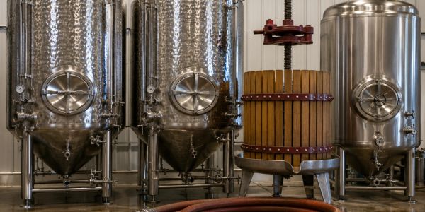 Metal brewing tanks and a wooden press inside a brewery.