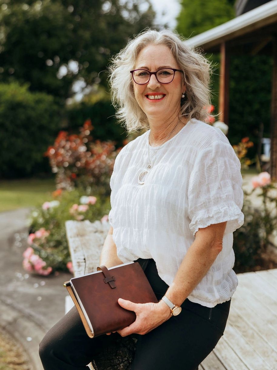 Whanganui Wedding Celebrant Prue sitting down outside holding her wedding notebook