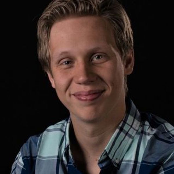 Young man smiling, wearing a blue plaid shirt.