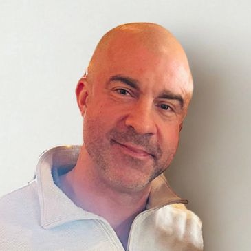 A smiling bald man with a light beard wearing a light-colored zip-up sweater.