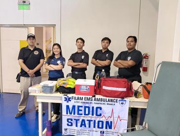 Five EMS medics stand behind a medic station table with medical supplies.