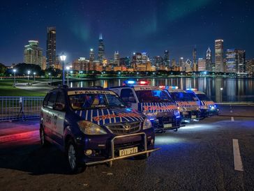 Police SUVs with flashing lights parked against a city skyline at night.