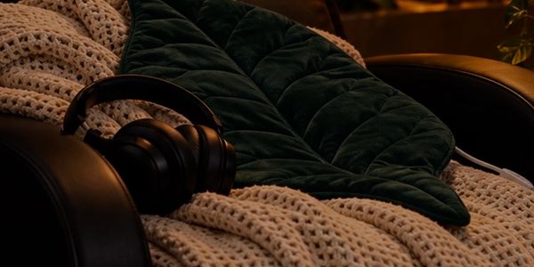 Headphones resting on a cozy blanket and cushion on a leather chair.