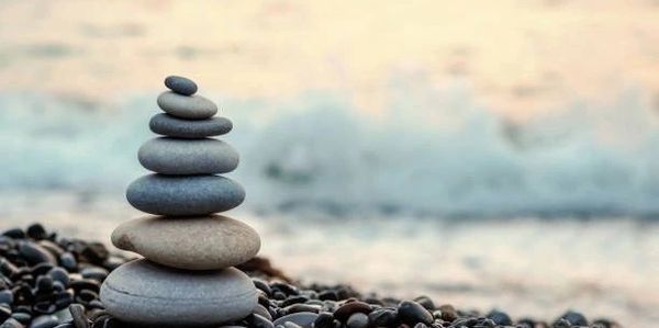Stacked stones on a pebble beach with ocean waves in the background.