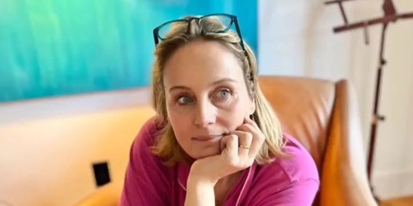 Woman in a pink shirt sitting thoughtfully on an orange chair with glasses on her head.